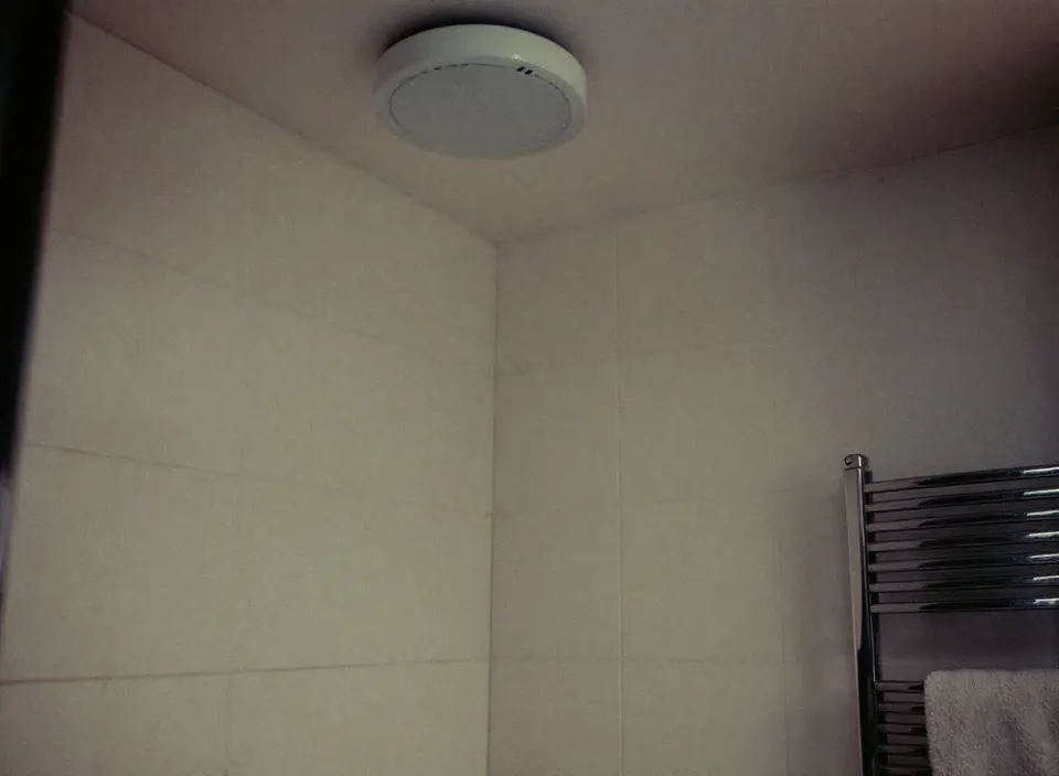 Hoek van een betegelde badkamer met een rond ventilatieventiel in het plafond en een handdoekradiator