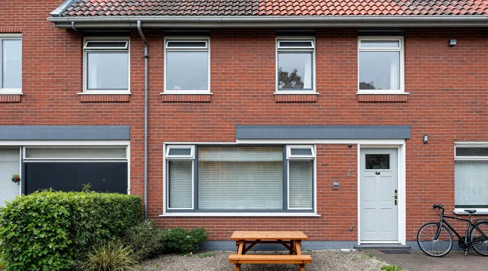 Gevel van een gerenoveerde rijwoning met nieuwe donkergrijze kozijnen en een smal ventilatierooster boven in elk kozijn